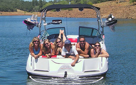A group of friends lying across the swim platform of a wakeboard boat on Collins Lake on a bright summer day.
