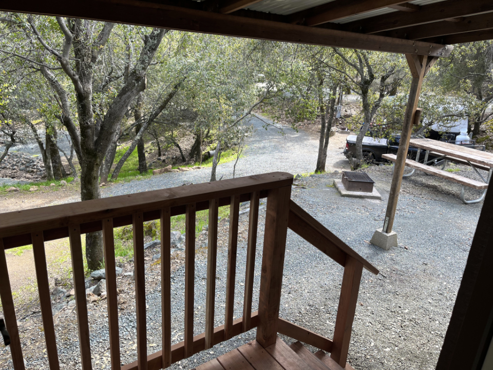 The view from a Collins Lake cabin porch across the gravel site to a picnic table and fire ring among the oaks.