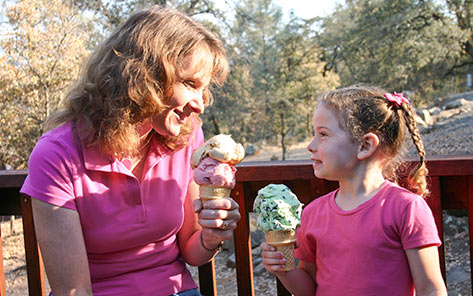 A woman and a young girl sitting on a deck at Collins Lake, each holding a very large ice cream cone.