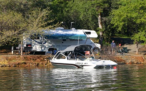 A motorhome parked on a lakefront campsite at Collins Lake with a ski boat moored on the water directly in front of it.