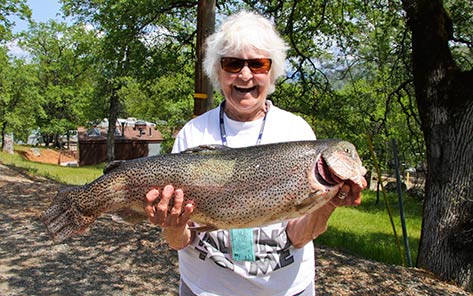 A smiling angler at Collins Lake holding a very large rainbow trout with both arms.
