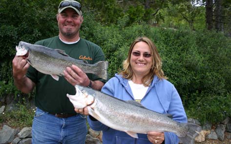 Two anglers at Collins Lake each holding up a large rainbow trout caught from the lake.